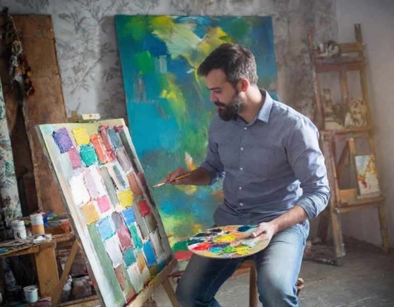 Künstler Ein Künstler malt an einer Staffelei mit bunter Farbpalette in einem Atelier.