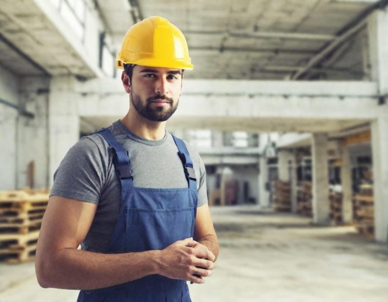 Handwerker Mann in Arbeitskleidung und Schutzhelm in einer Lagerhalle.